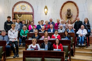 Radni sesji sejmiku siedzą w ławkach i pozują do zdjęcia grupowego.