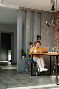 Kobieta na wózku inwalidzkim siedząca przy biurku i korzystająca z laptopa
