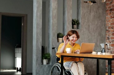 Kobieta na wózku inwalidzkim siedząca przy biurku i korzystająca z laptopa