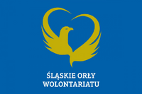 Logo inicjatywy Śląskie Orły Wolontariatu na niebieskim tle. W centrum znajduje się stylizowany złoty orzeł z rozpostartymi skrzydłami, które tworzą kształt serca. Pod grafiką widnieje biały napis: ‘ŚLĄSKIE ORŁY WOLONTARIATU’