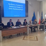 Panel dyskusyjny podczas spotkania Powiatowej Społecznej Rady ds. Osób Niepełnosprawnych, z uczestnikami siedzącymi przy stole i prezentacją na ekranie.