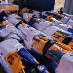 Zestaw upominków promocyjnych zawiniętych w białe materiały z niebieskimi wstążkami i żółtymi długopisami, ułożonych na stole.