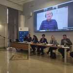 Panel uczestników siedzących przy stole podczas spotkania, z dużym ekranem w tle wyświetlającym transmisję wideo z wystąpienia Pełnomocnika Rządu ds. Osób Niepełnosprawnych Pana Łukasza Krasonia