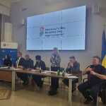 Panel uczestników spotkania Powiatowej Społecznej Rady ds. Osób Niepełnosprawnych, z osobą przemawiającą i slajdem z logo PFRON na ekranie w tle