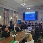 Spotkanie z Powiatowymi Społecznymi Radami ds. Osób Niepełnosprawnych w sali konferencyjnej, uczestnicy siedzą przy stołach, a osoba przemawia przy ekranie z prezentacją w tle