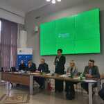 Pani Bożena Borowiec Zastępca Prezesa Zarządu PFRON, przemawiająca przy stole podczas spotkania, na ekranie w tle zielony slajd z logo Państwowego Funduszu Rehabilitacji Osób Niepełnosprawnych.