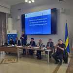 Członek Zarządu Województwa Śląskiego Pan Rafał Adamczyk przemawiający przy stole podczas spotkania w sali konferencyjnej, na ekranie w tle widoczny slajd z napisem: ‘Spotkanie z Powiatowymi Społecznymi Radami ds. Osób Niepełnosprawnych