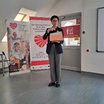 Kobieta stoi w sali szkoleniowej i przemawia do uczestników, trzyma w ręce notes. Za nią stoją roll-upy Regionalnej Fundacji Pomocy Niewidomym oraz Specjalistycznego Centrum Wspierającego Edukację Włączającą w Ziemięcicach