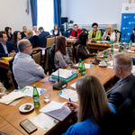 Uczestnicy spotkania siedzą wokół stołów ustawionych w kształt podkowy w sali konferencyjnej.