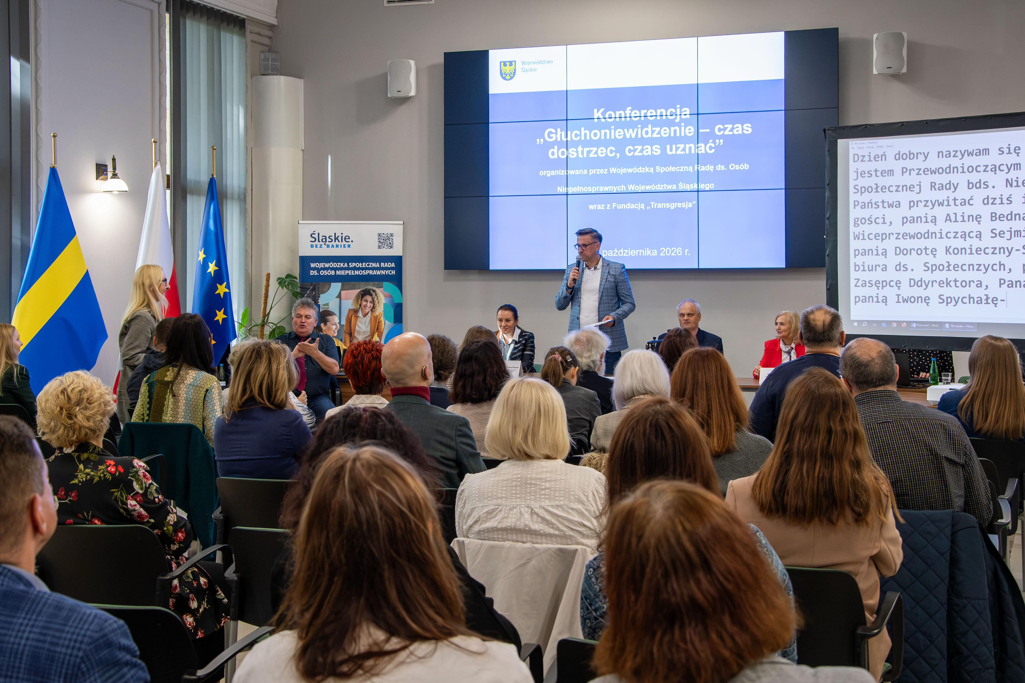 Pan Tomasz Ciesielski wita uczestników konferencji. w tle slajd z tytułem konferencji.