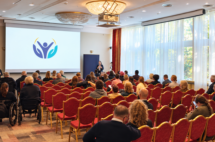 Sala konferencyjna, z uczestnikami konferencji oraz osobą występującą.